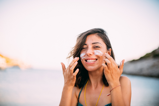 Woman at the beach smiling while applying sunscreen