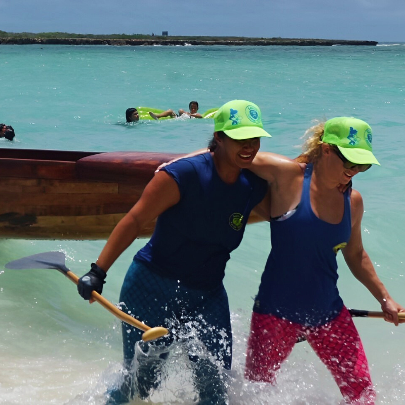 Photo of two friends smiling and helping each other out of the ocean after kayaking