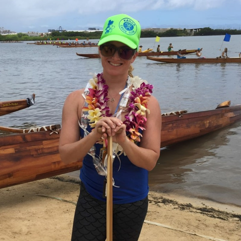 Michelle, owner of Gypsea Mafia, wearing Kailua Canoe Club hat standing with a paddle